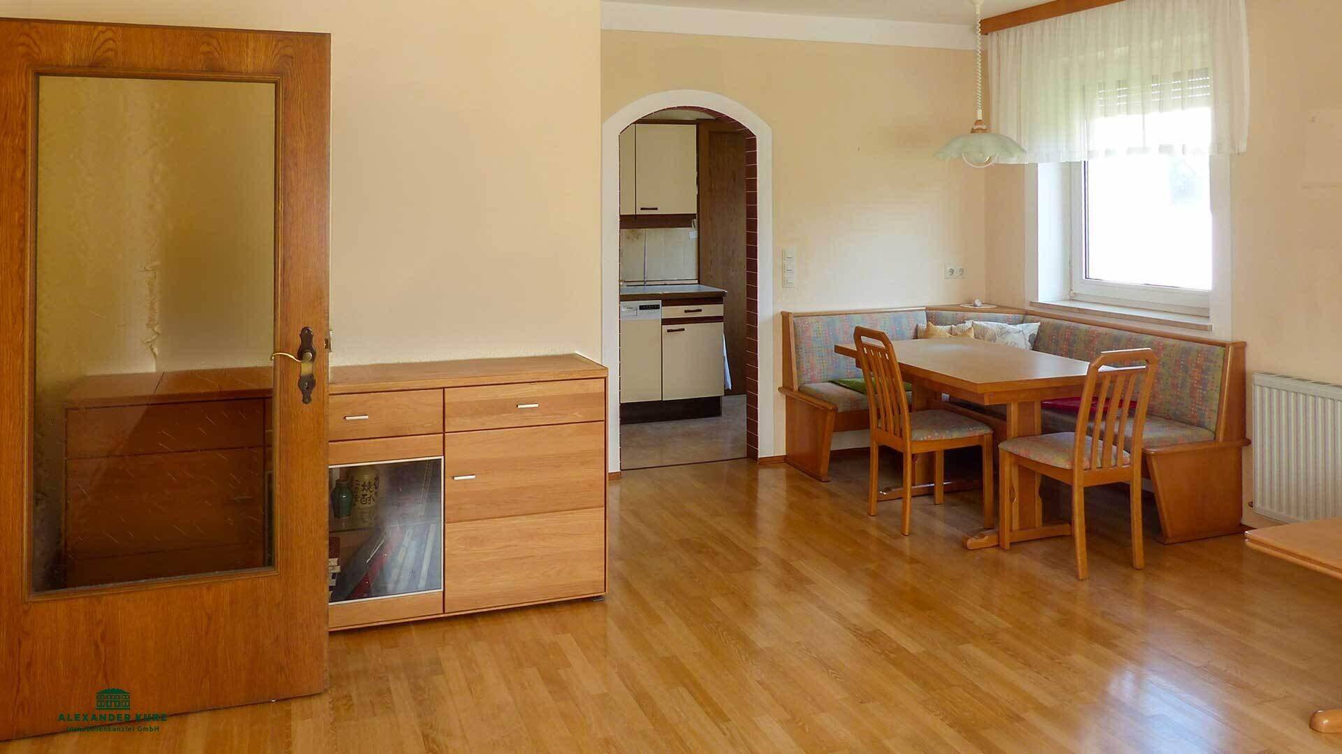 Gemütlicher Essbereich mit Holztisch und Eckbank, angrenzend an eine kleine Küche.