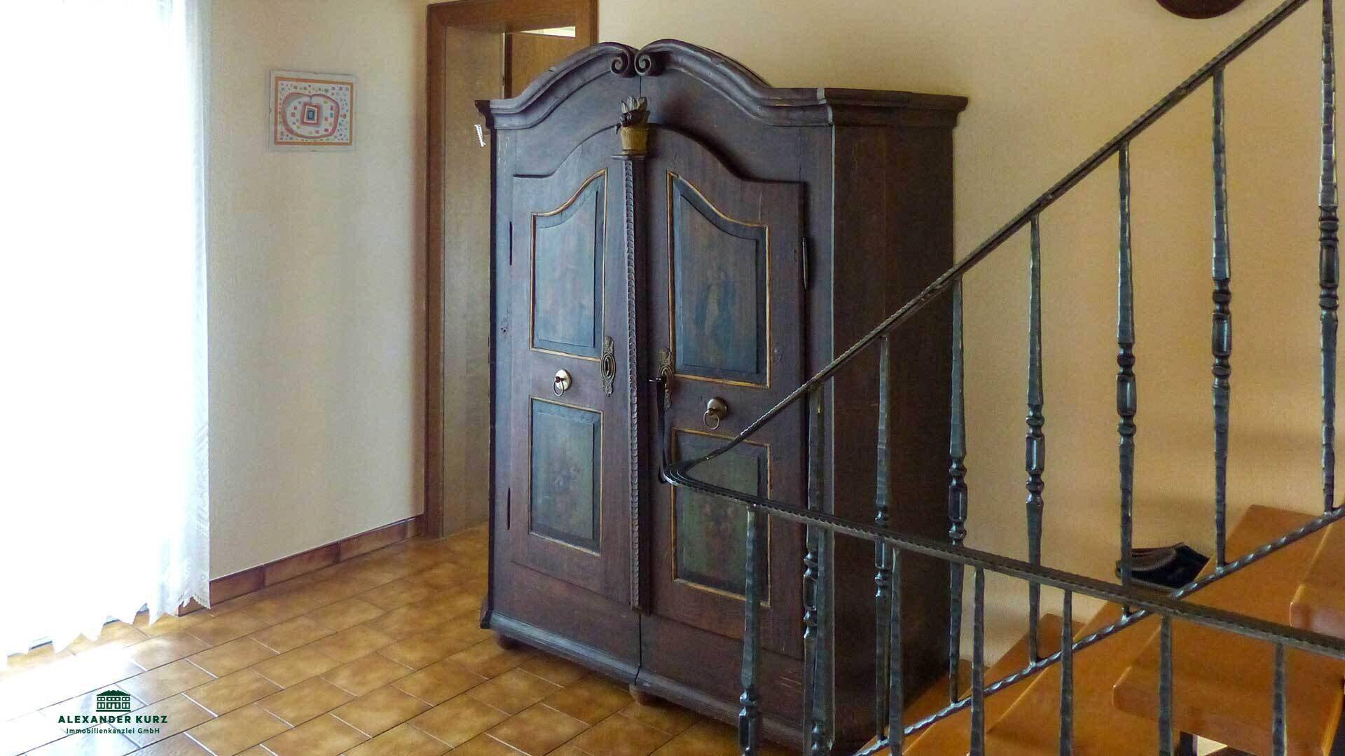 Flur mit traditionellem Holzschrank und Treppe, gefliestem Boden und hellem Licht.