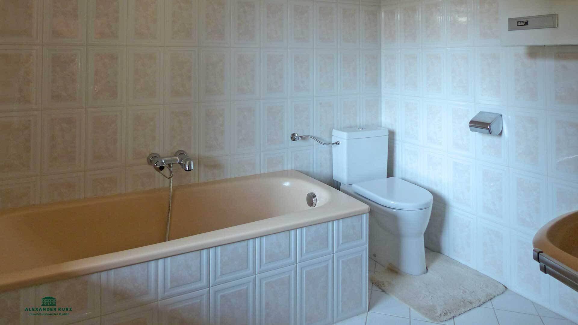 Badezimmer mit beiger Badewanne, WC und hellen Fliesen an Wänden und Boden.
