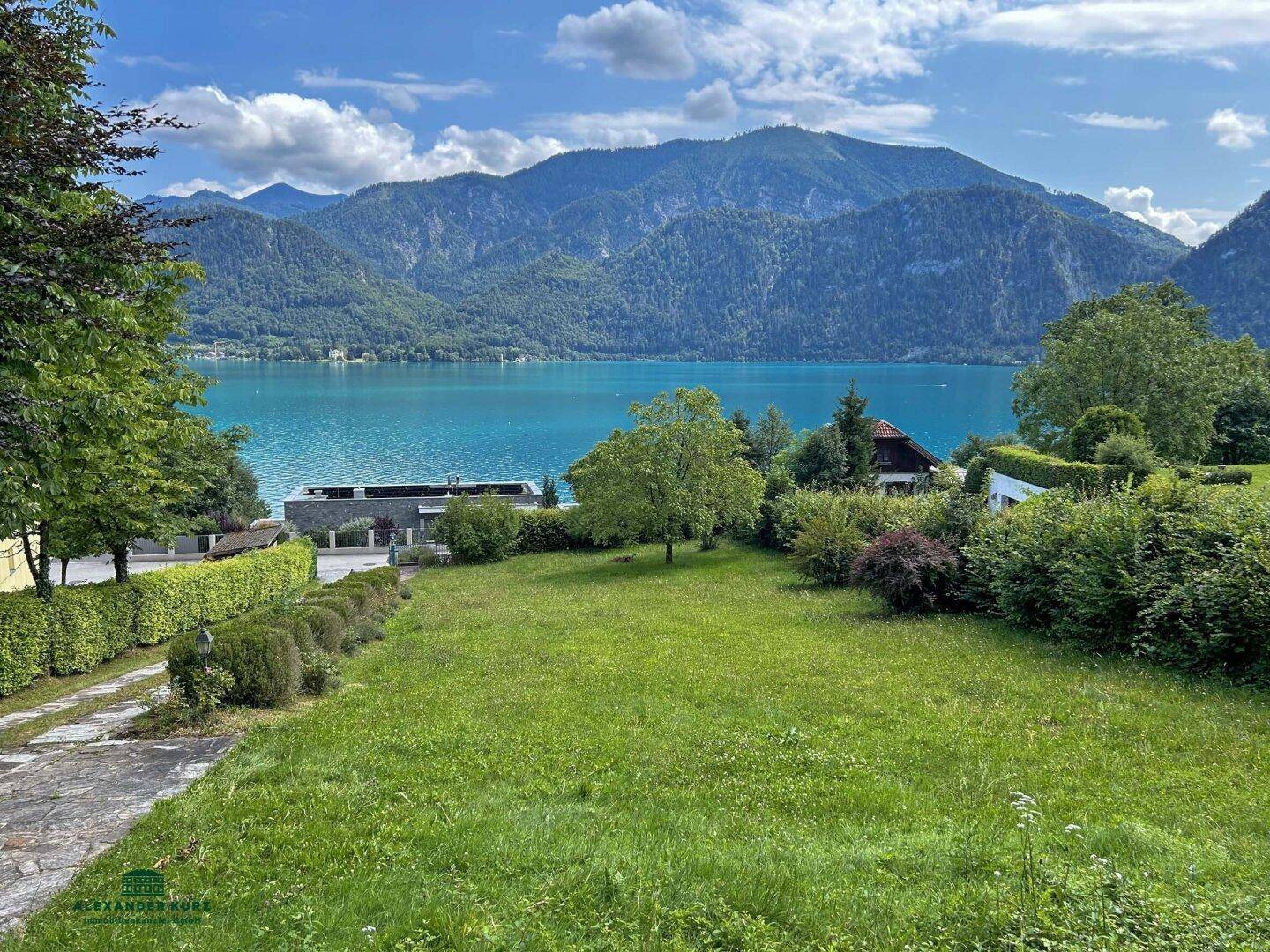 Weitläufiger Gartenbereich mit Rasenfläche und Panoramablick auf den See und die Berge.