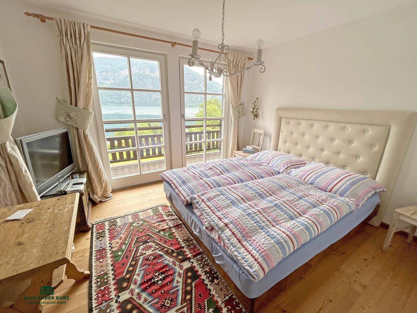 Gemütliches Schlafzimmer mit Doppelbett, Teppich und Zugang zum Balkon mit Seeblick.