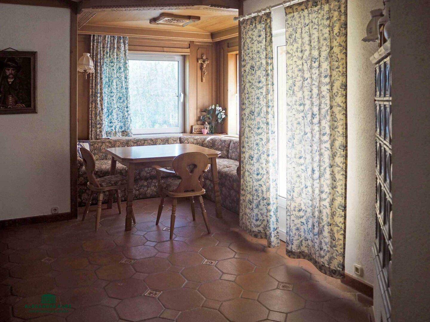 Traditioneller Essbereich mit Holztäfelung, Eckbank und Terrakottafliesen, hell durch großes Fenster.