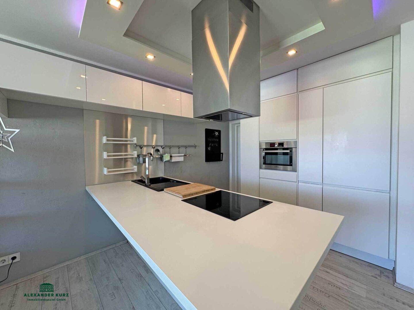 Elegante, moderne Küche mit weißer Arbeitsplatte, Induktionskochfeld und Dunstabzugshaube.