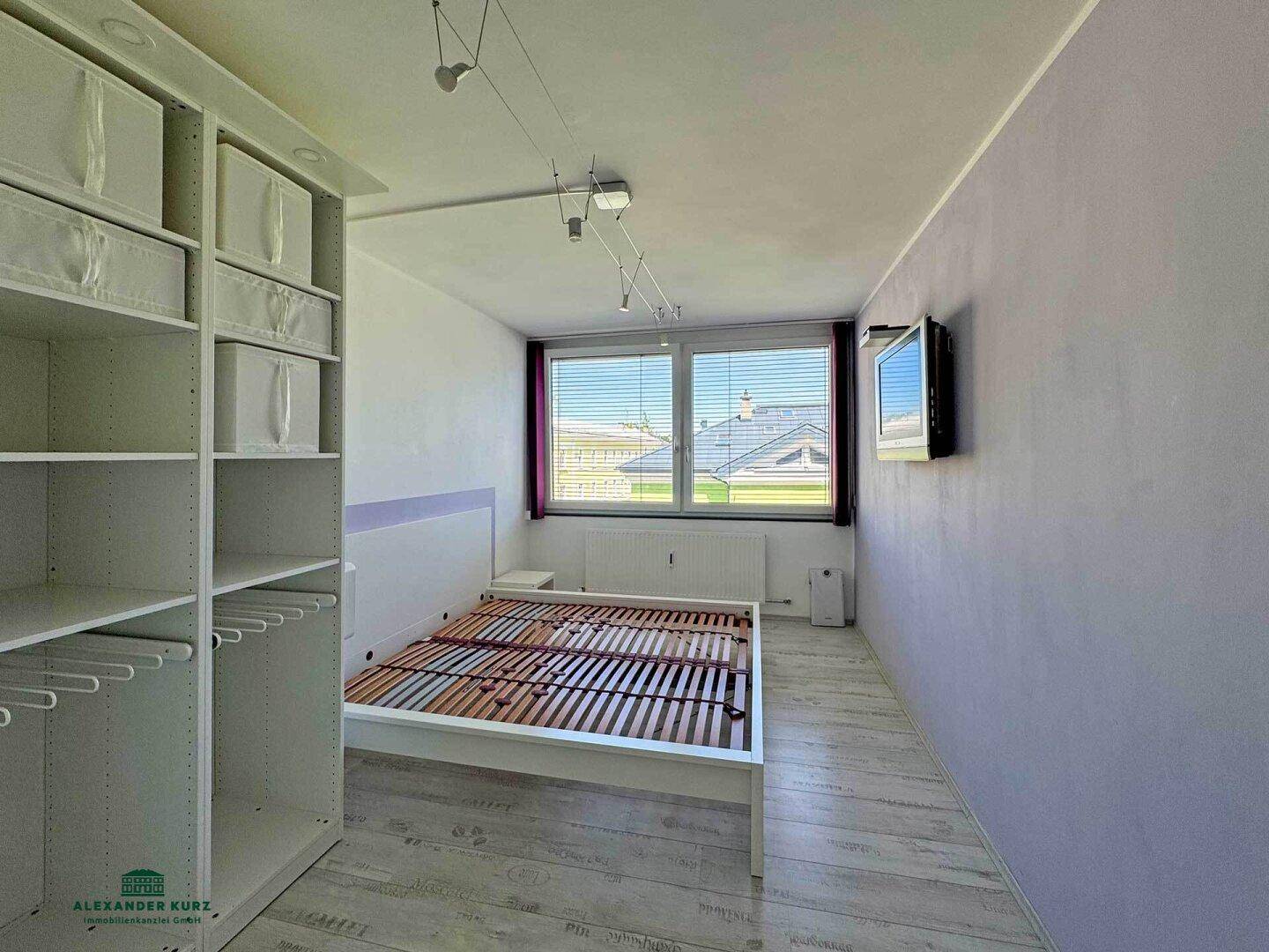 Schlafzimmer mit hellem Laminatboden, großem Fenster und integriertem Kleiderschrank.