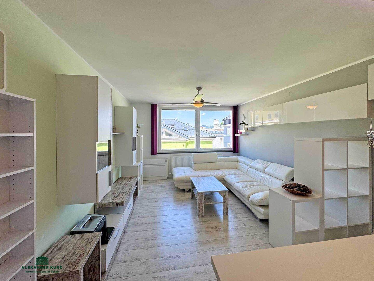 Heller Wohnbereich mit bequemer weißer Couch, Regalen und Blick auf die Umgebung.