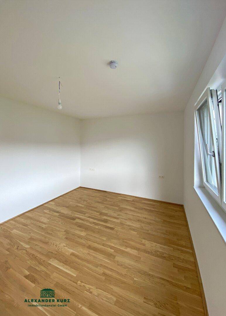 Freundliches Zimmer mit hellem Parkettboden und einem Fenster für viel Tageslicht.