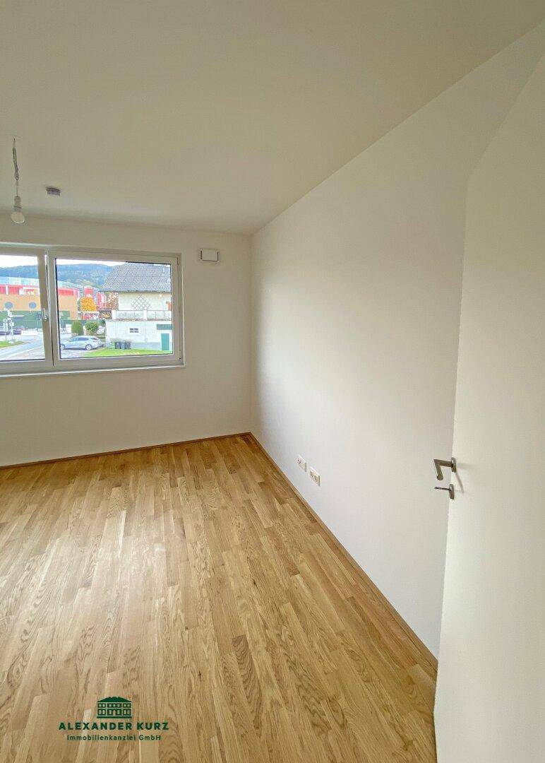 Helles Zimmer mit Parkettboden und Fenster, das einen Blick auf die Straße bietet.