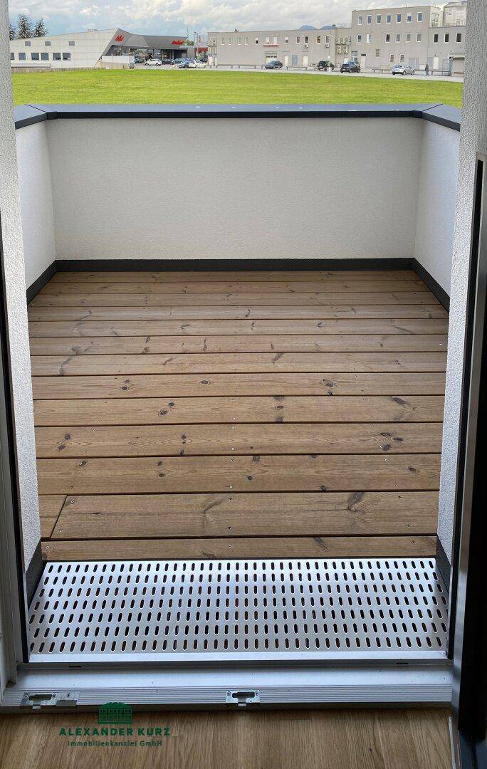 Kleiner Balkon mit Holzboden und Blick auf die umliegende Bebauung und Parkplätze.