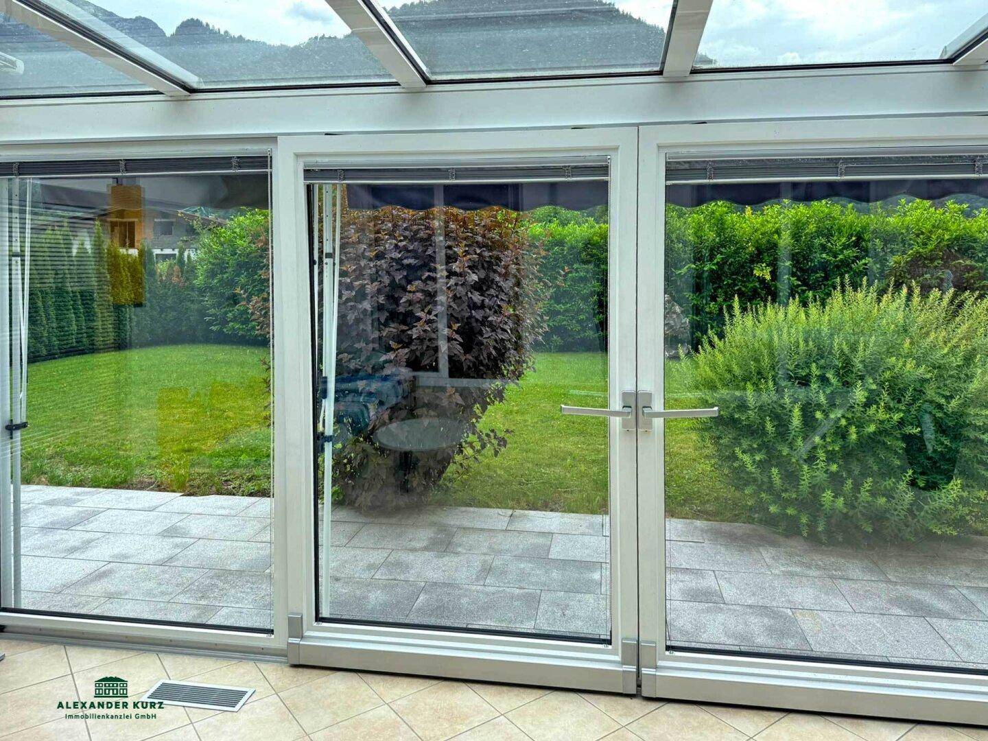 Heller Wintergarten mit Glasdach und Blick auf den grünen Gartenbereich.