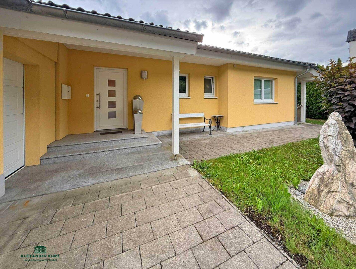 Freundlicher Hauseingang mit gelber Fassade, gepflastertem Weg und kleinem Vorgarten.