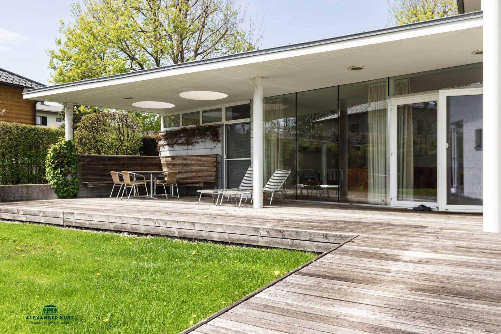 Moderne Architektur mit großer Holzterrasse, Liegestühlen und Blick ins Grüne.