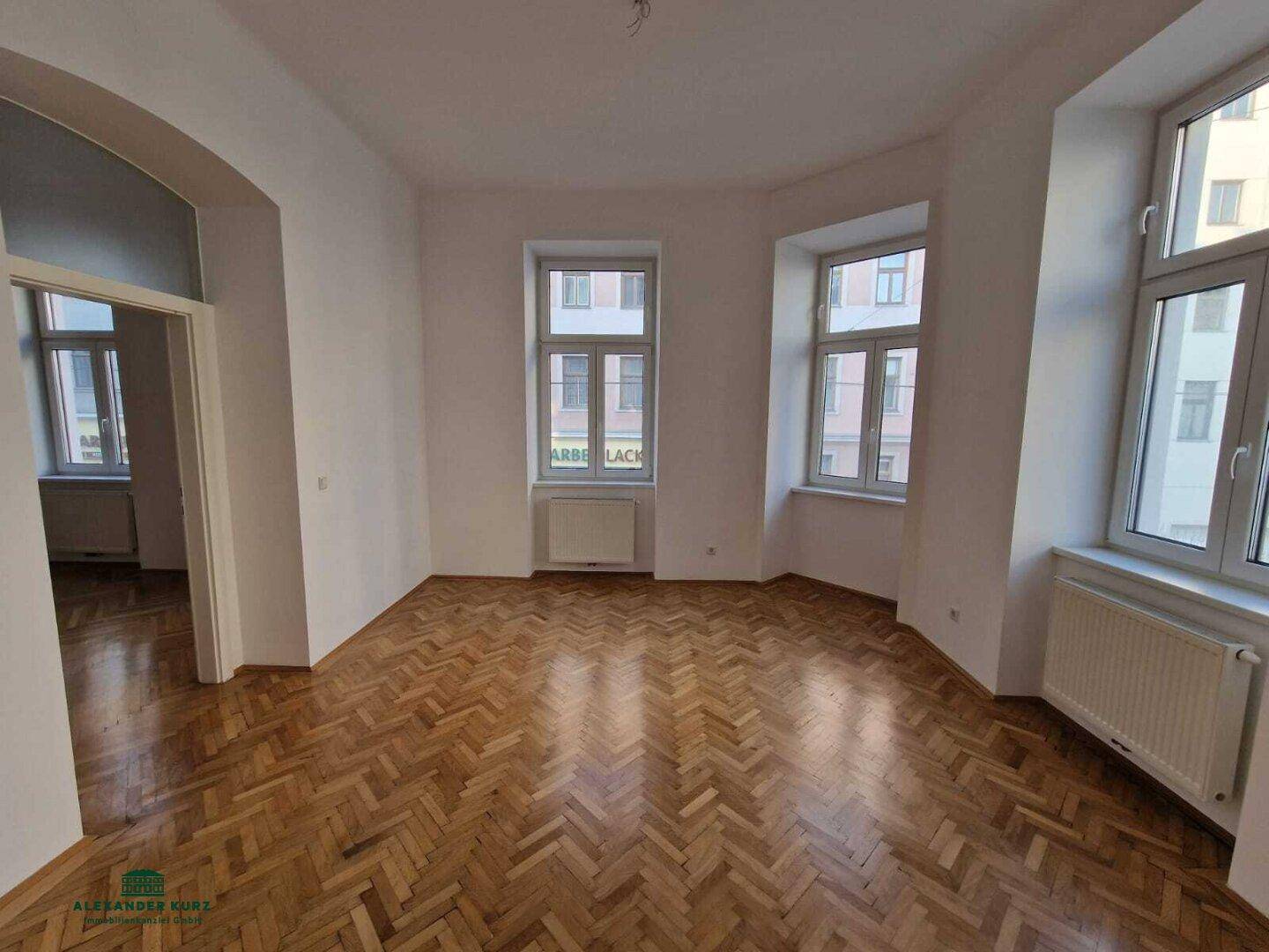 Geräumiges Zimmer mit Fischgrätparkett, vielen Fenstern und Blick auf die Stadt.