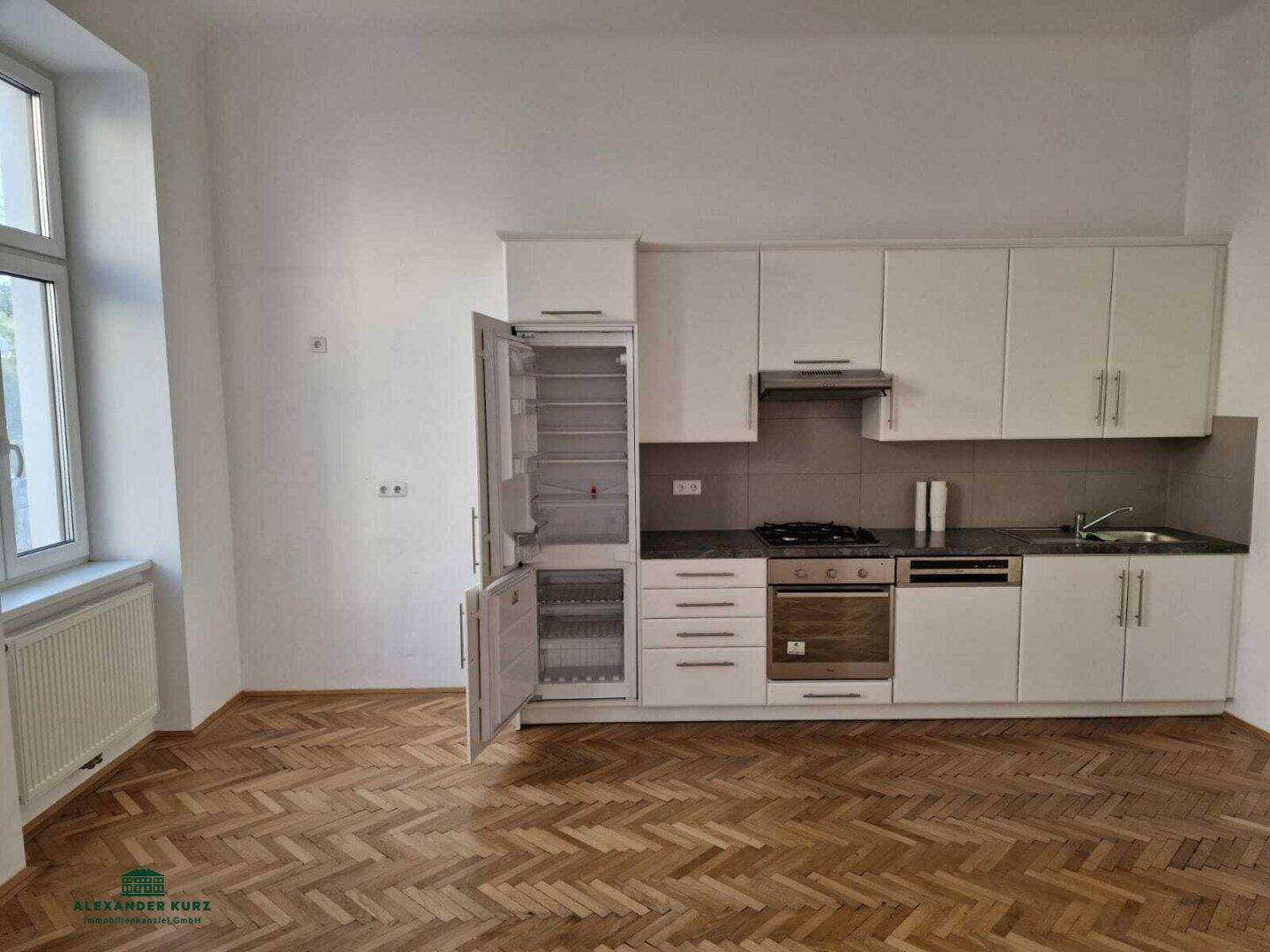 Neuwertige Einbauküche mit weißen Schränken, dunkler Arbeitsplatte und integrierten Geräten.