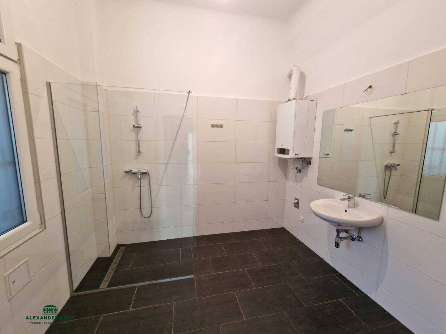 Modernes Badezimmer mit großer ebenerdiger Dusche, dunklen Bodenfliesen und Fenster.