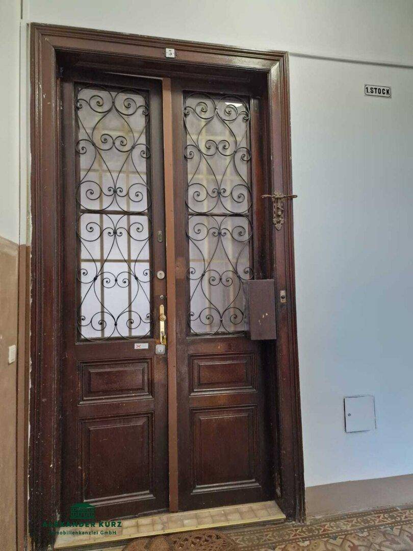 Historische Wohnungstür mit schmiedeeisernen Verzierungen im Treppenhaus des Altbaus.