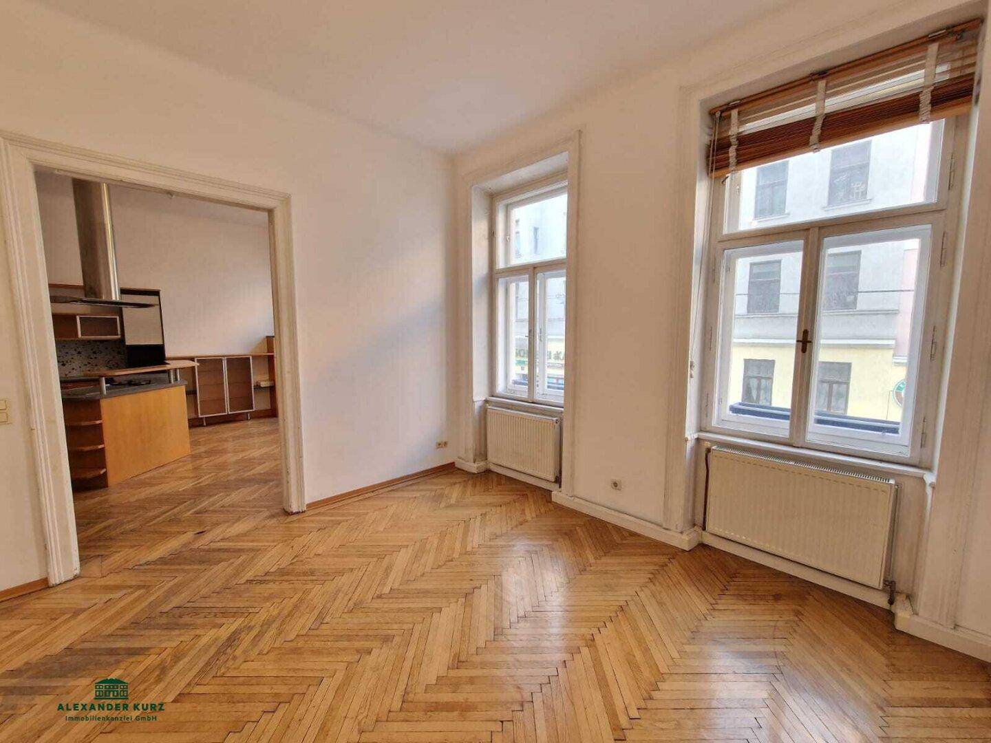 Helles Wohnzimmer mit Fischgrätparkett und Zugang zu einer geräumigen Küche.