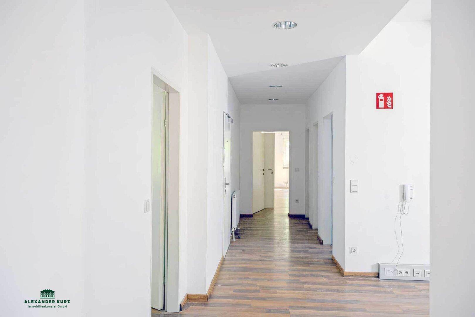 Heller Flur mit Holzboden, weißen Wänden und mehreren Türen, die zu weiteren Räumen führen.