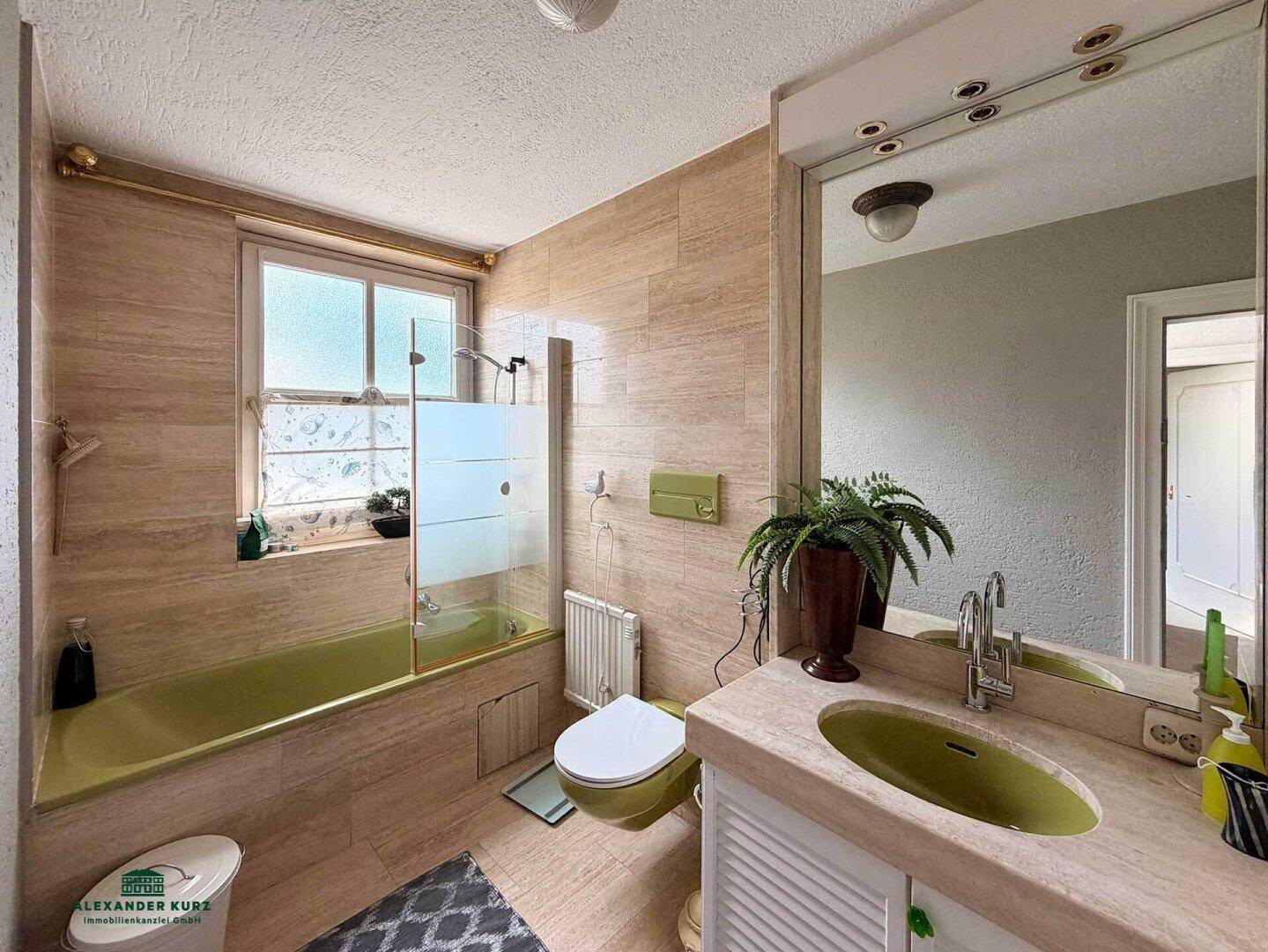 Badezimmer im Stil der 80er Jahre mit grüner Badewanne, Waschbecken und WC, umgeben von beigefarbenen Fliesen.