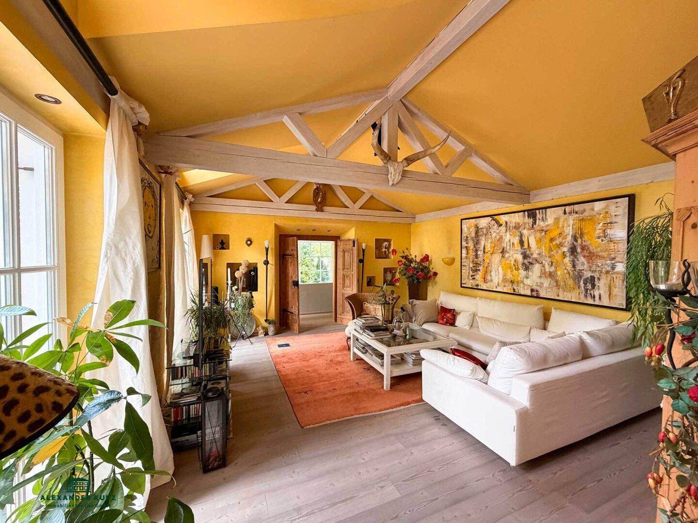Helles Wohnzimmer mit gelben Wänden, sichtbaren Dachbalken, weißem Sofa und einem großen Kunstwerk.