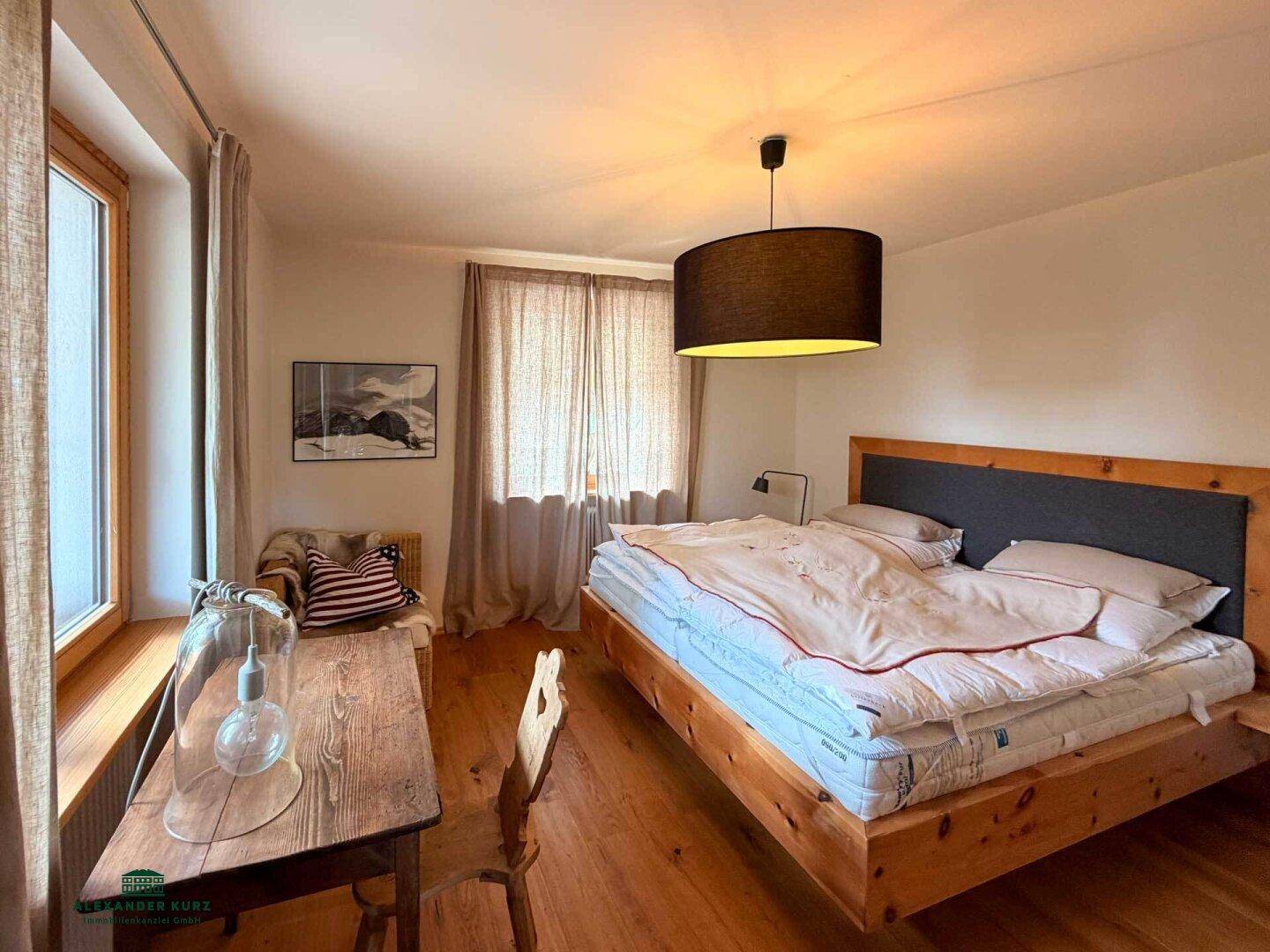 Helles Schlafzimmer mit Holzboden, großem Holzbett und viel Tageslicht durch die Fenster.
