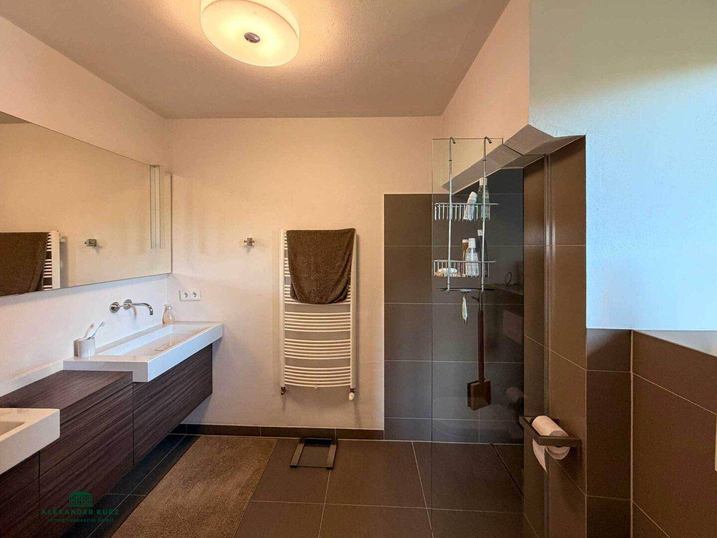 Modernes Badezimmer mit Doppelwaschbecken, großem Spiegel, beheiztem Handtuchhalter und begehbarer Dusche.