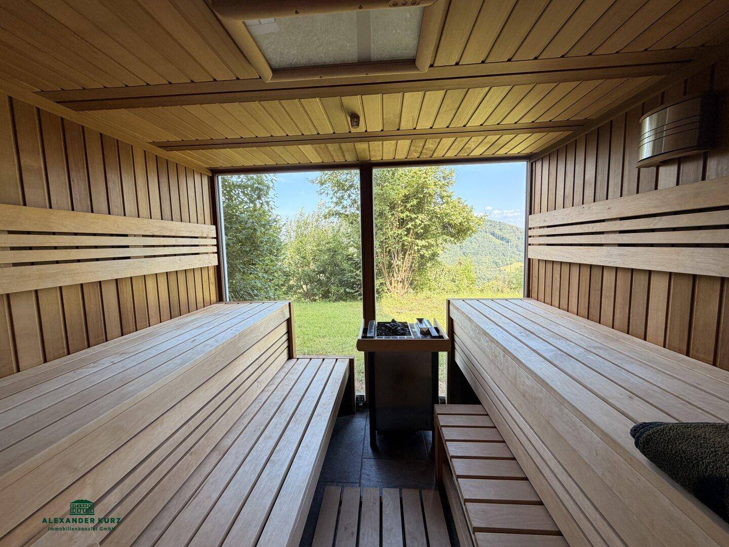 Helle Sauna mit Holzverkleidung, bequemen Bänken und Panoramablick in die grüne Landschaft.