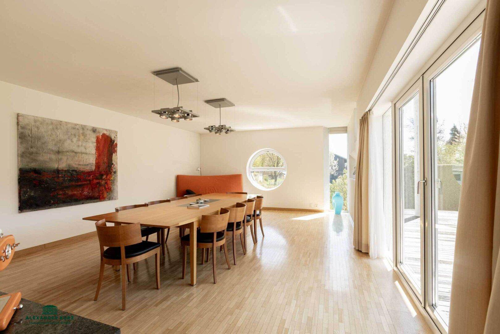 Helles Esszimmer mit großem Holztisch, modernen Leuchten und Zugang zum Balkon.