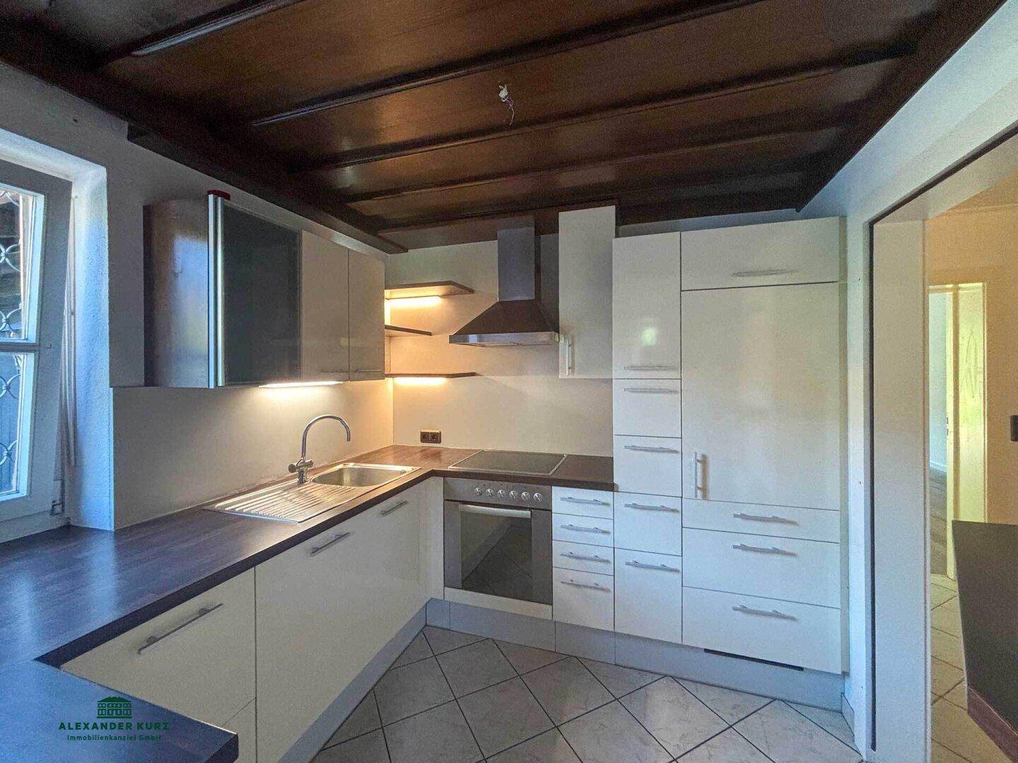 Moderne Küche mit weißen Schränken, Holzarbeitsplatte, Fliesenboden und sichtbaren Deckenbalken.