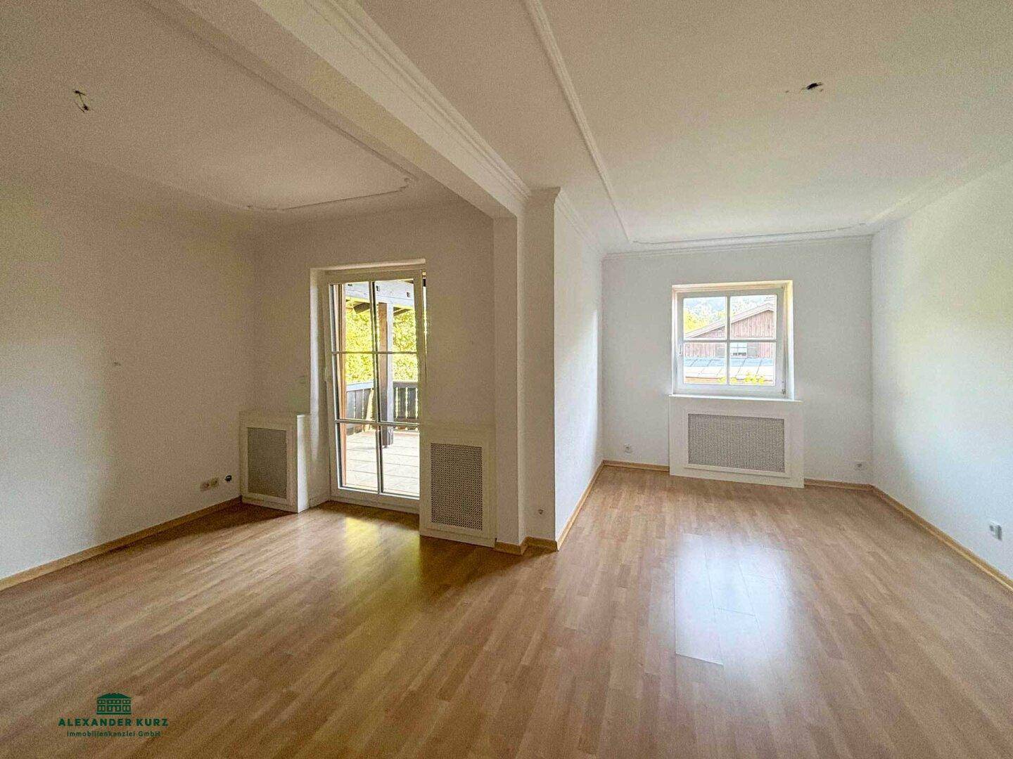 Heller Wohnbereich mit Holzboden, weißen Wänden und Zugang zu einem Außenbereich.