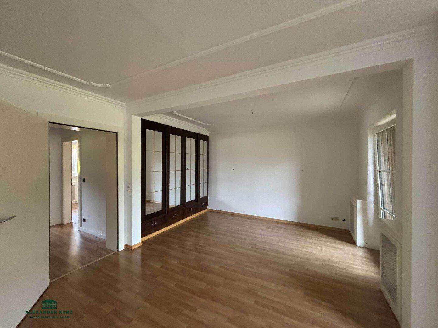 Geräumiger Wohnbereich mit Holzboden, weißen Wänden und integrierten Holzschränken.