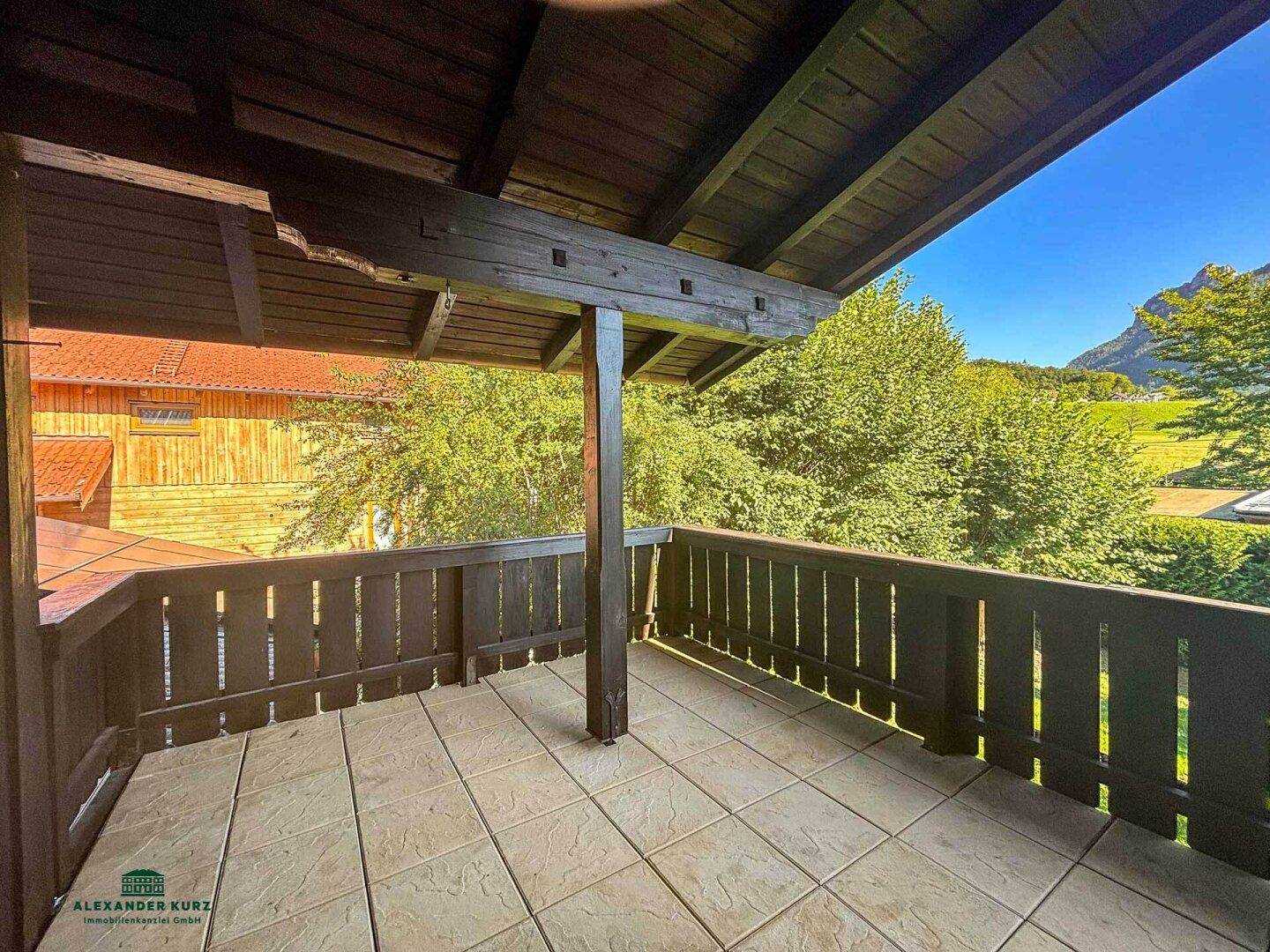 Geräumiger Balkon mit Fliesenboden, Holzgeländer und weitem Blick auf die Berge.