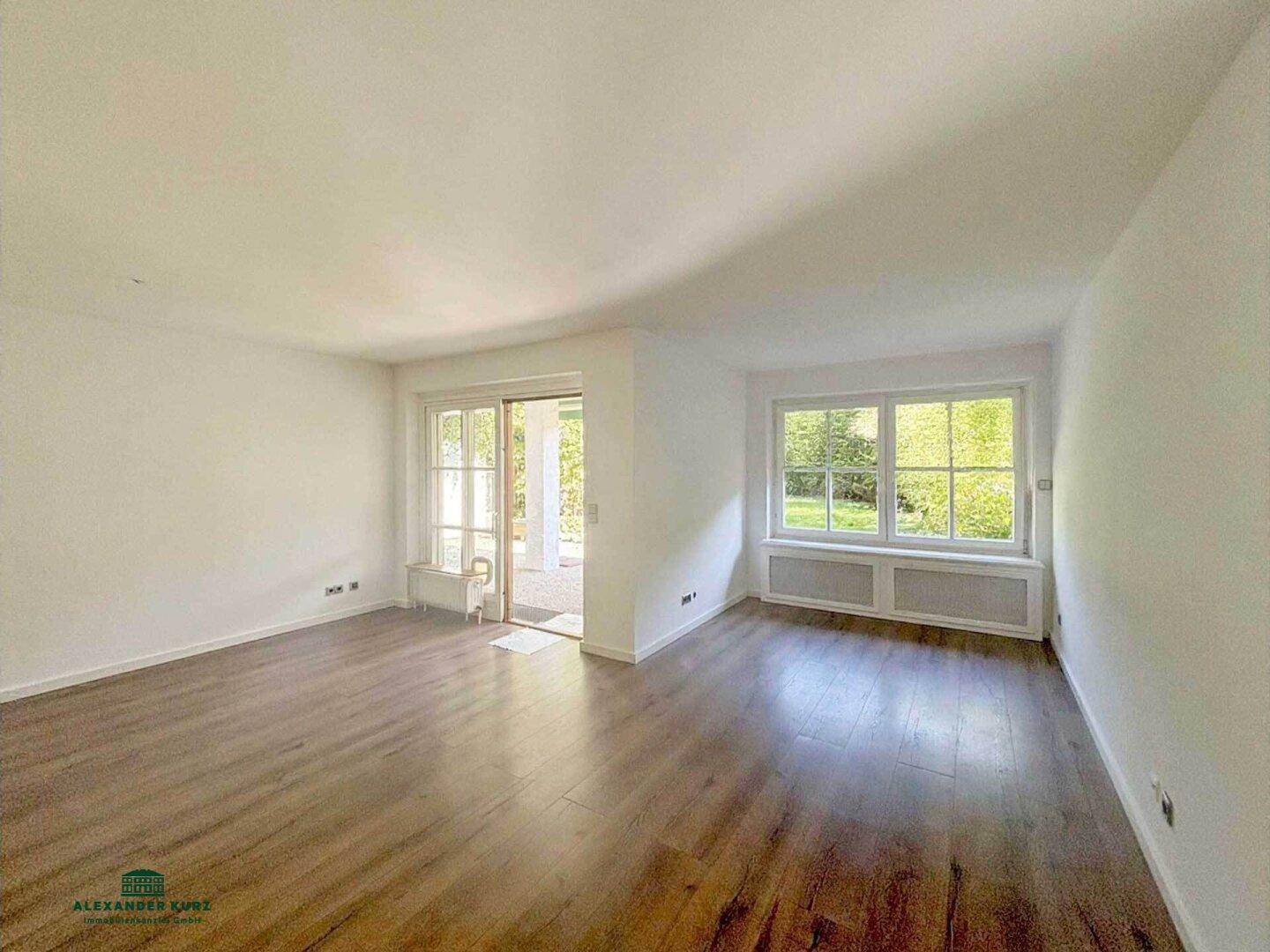 Heller Wohnraum mit Laminatboden, großen Fenstern und Zugang zum Außenbereich.