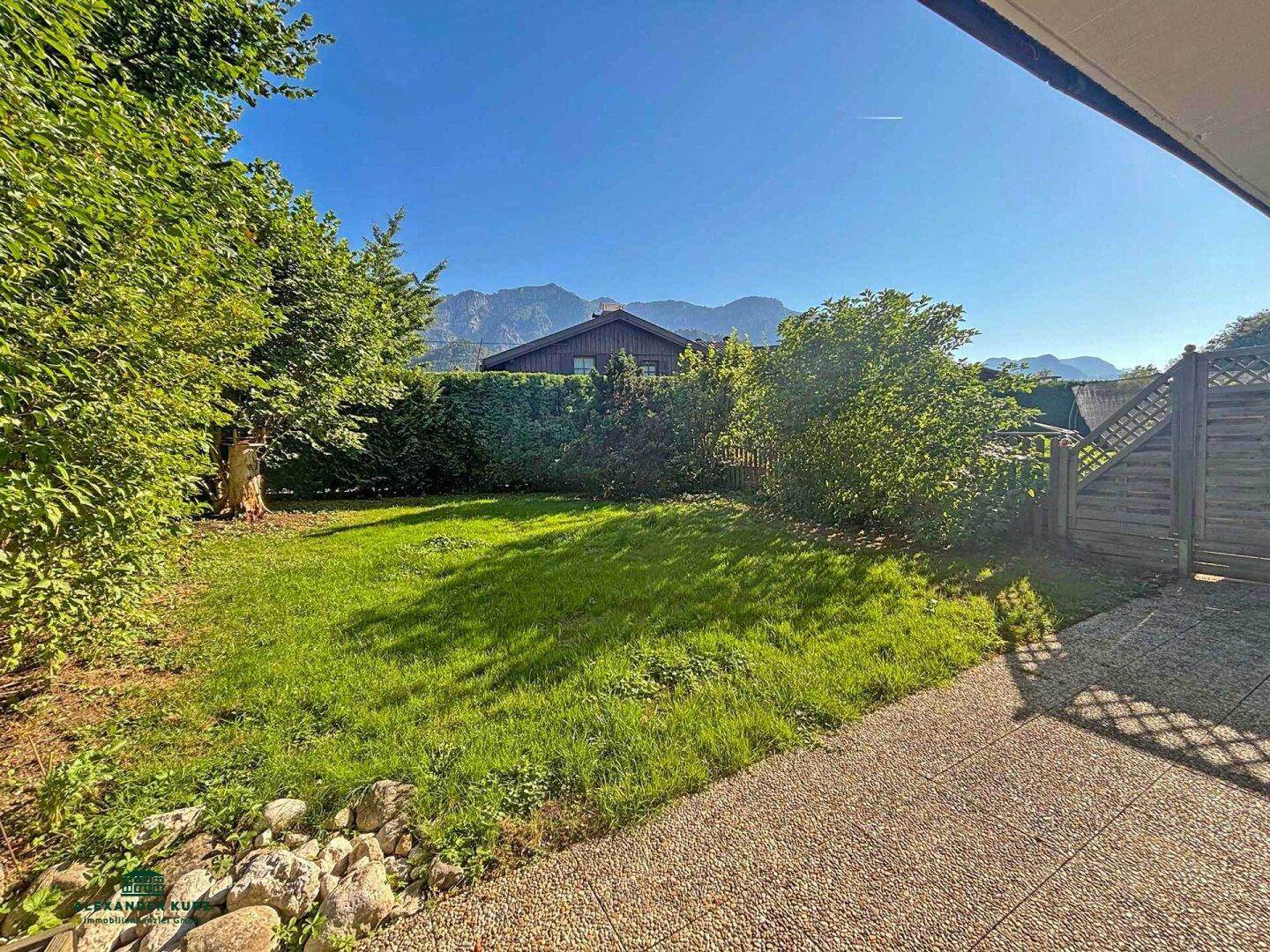Sonniger Gartenbereich mit Rasenfläche, Hecke und Blick auf die umliegenden Berge.