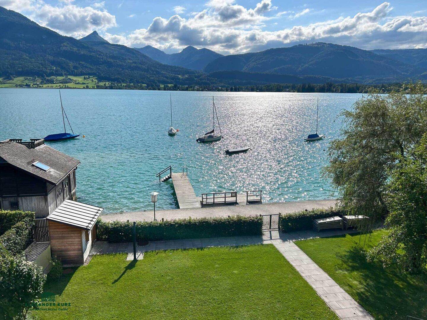 Gartenbereich mit direktem Seezugang und privatem Steg, umgeben von einer malerischen Berglandschaft.
