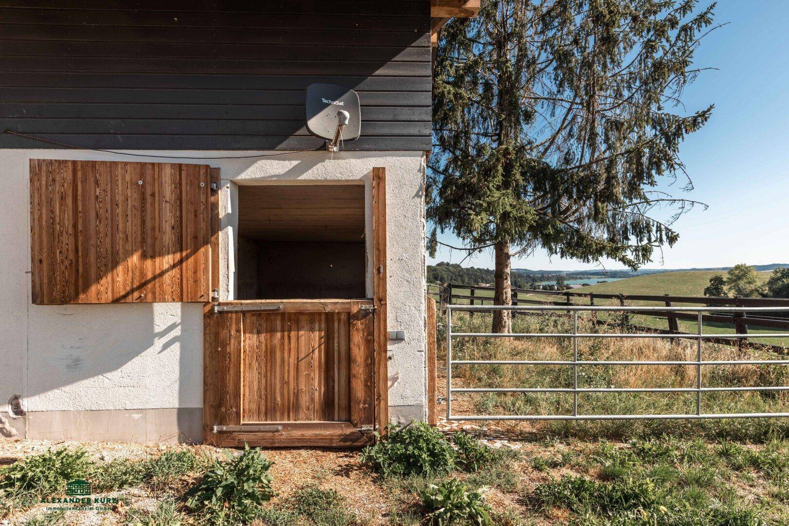 Stalltür aus Holz an einem Gebäude mit Blick auf einen See und grüne Landschaft in der Ferne.