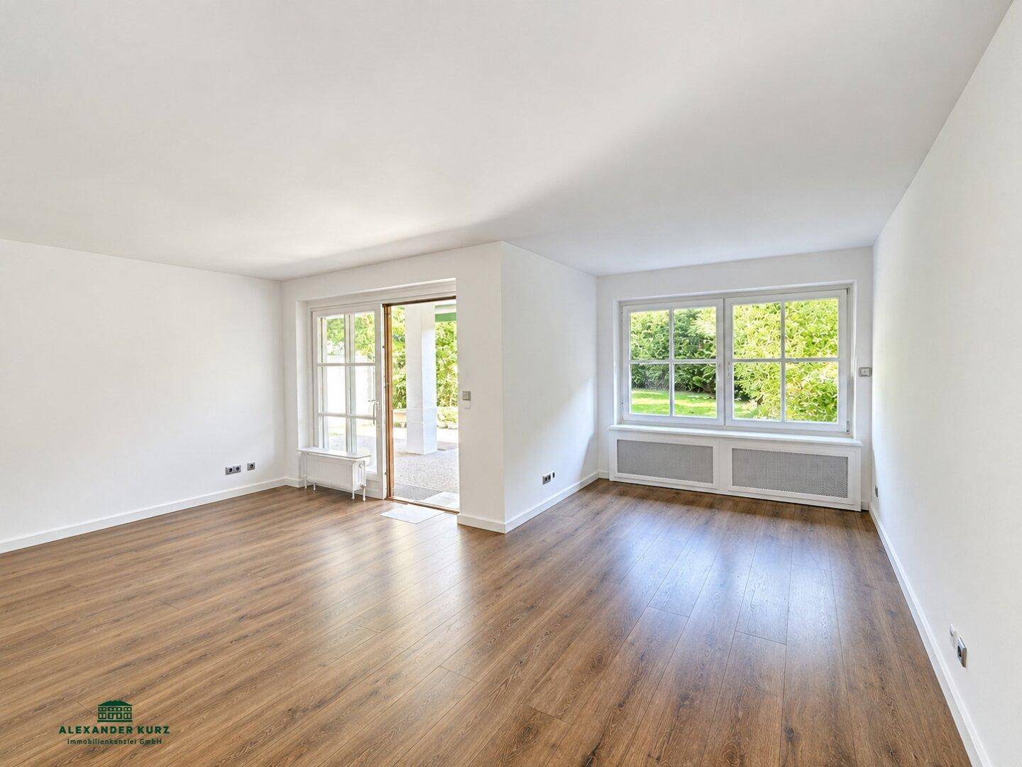 Helles Wohnzimmer mit Laminatboden, großen Fenstern und Zugang zu einem Außenbereich.