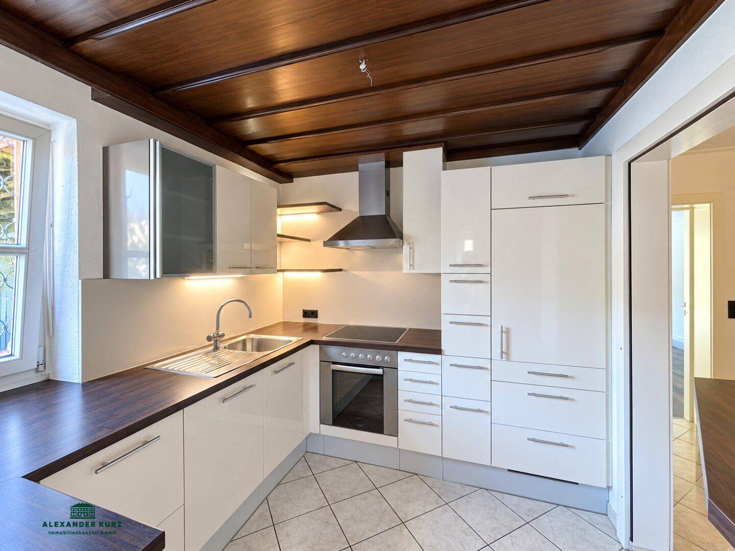 Moderne Küche mit weißen Hochglanzschränken, dunkler Arbeitsplatte und Holzbalkendecke.