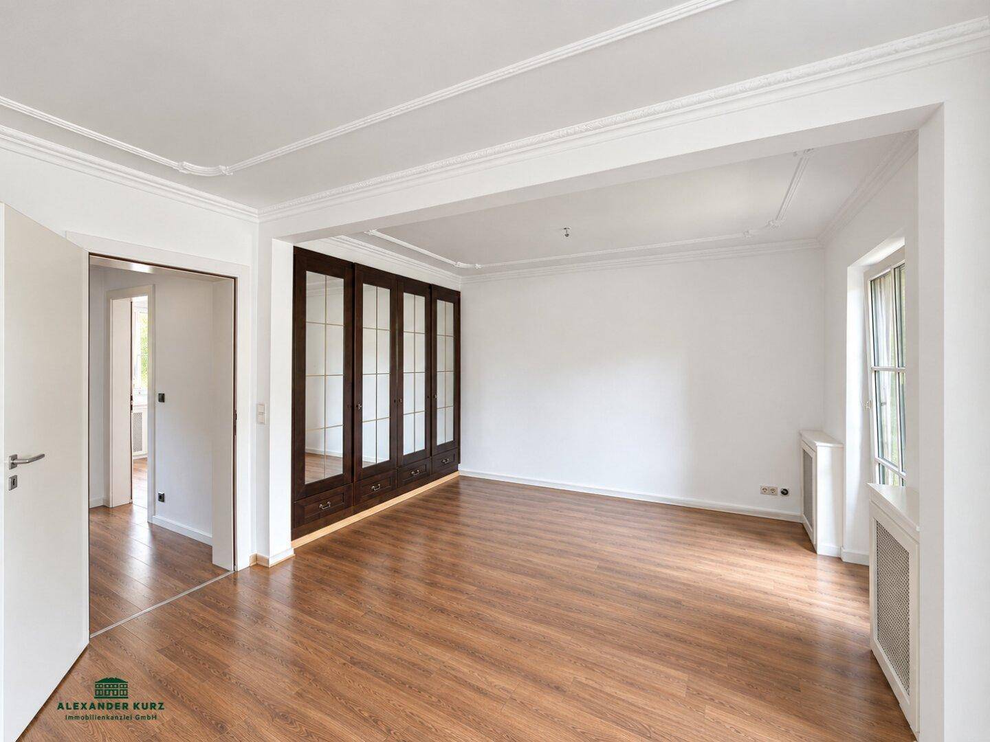 Geräumiger Wohnbereich mit Laminatboden, integrierten Schränken und dekorativen Deckenleisten.