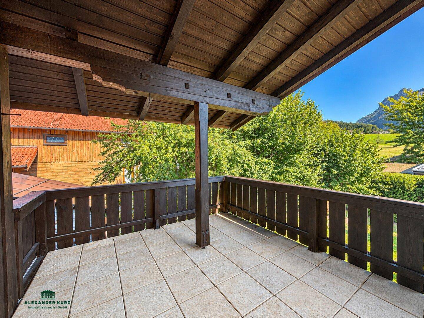 Großer Holzbalkon mit Fliesenboden und weitem Blick auf die umliegende Berglandschaft.