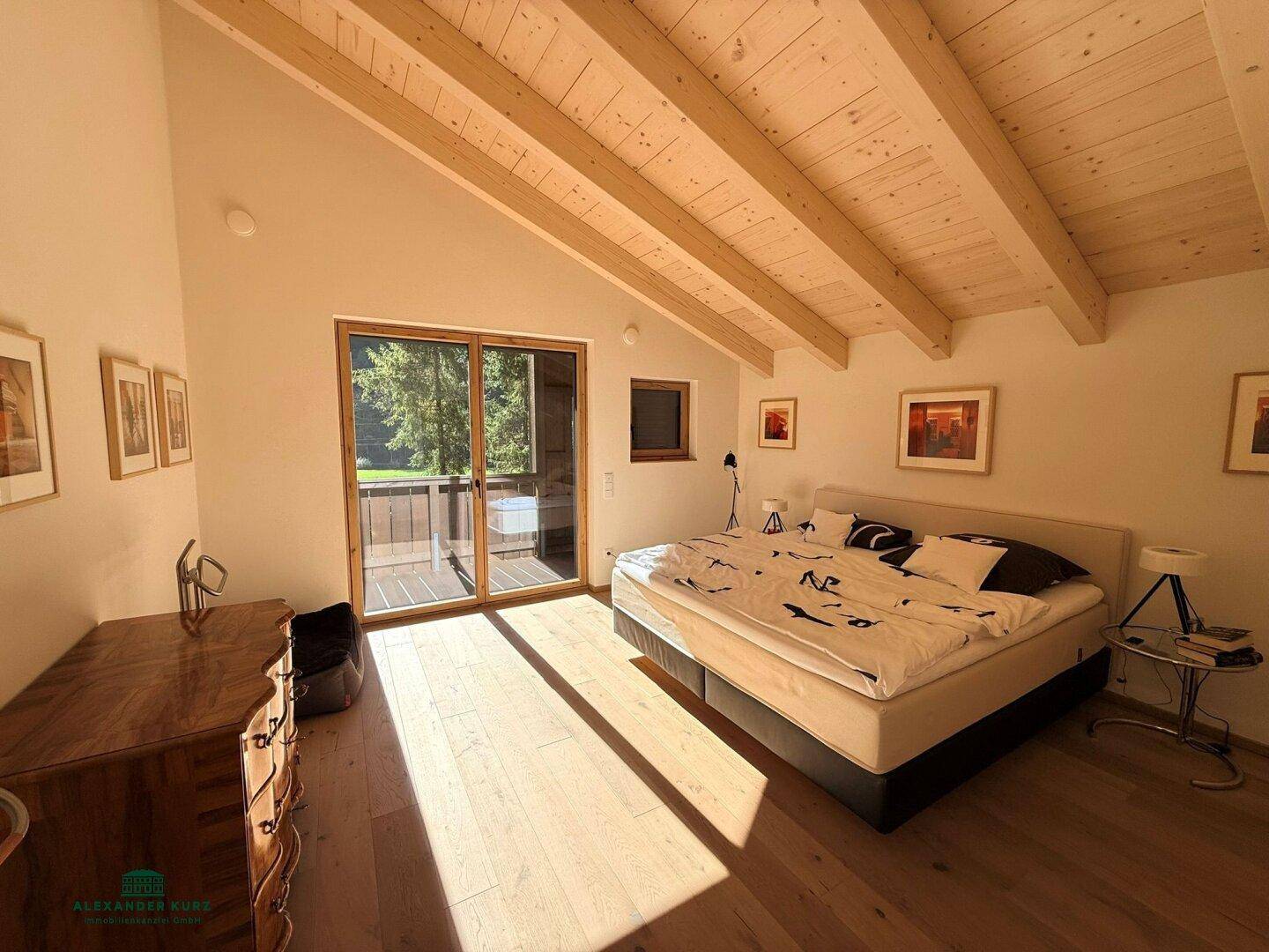 Helles Schlafzimmer mit Holzbalkendecke, Parkettboden und Zugang zu einem Balkon.
