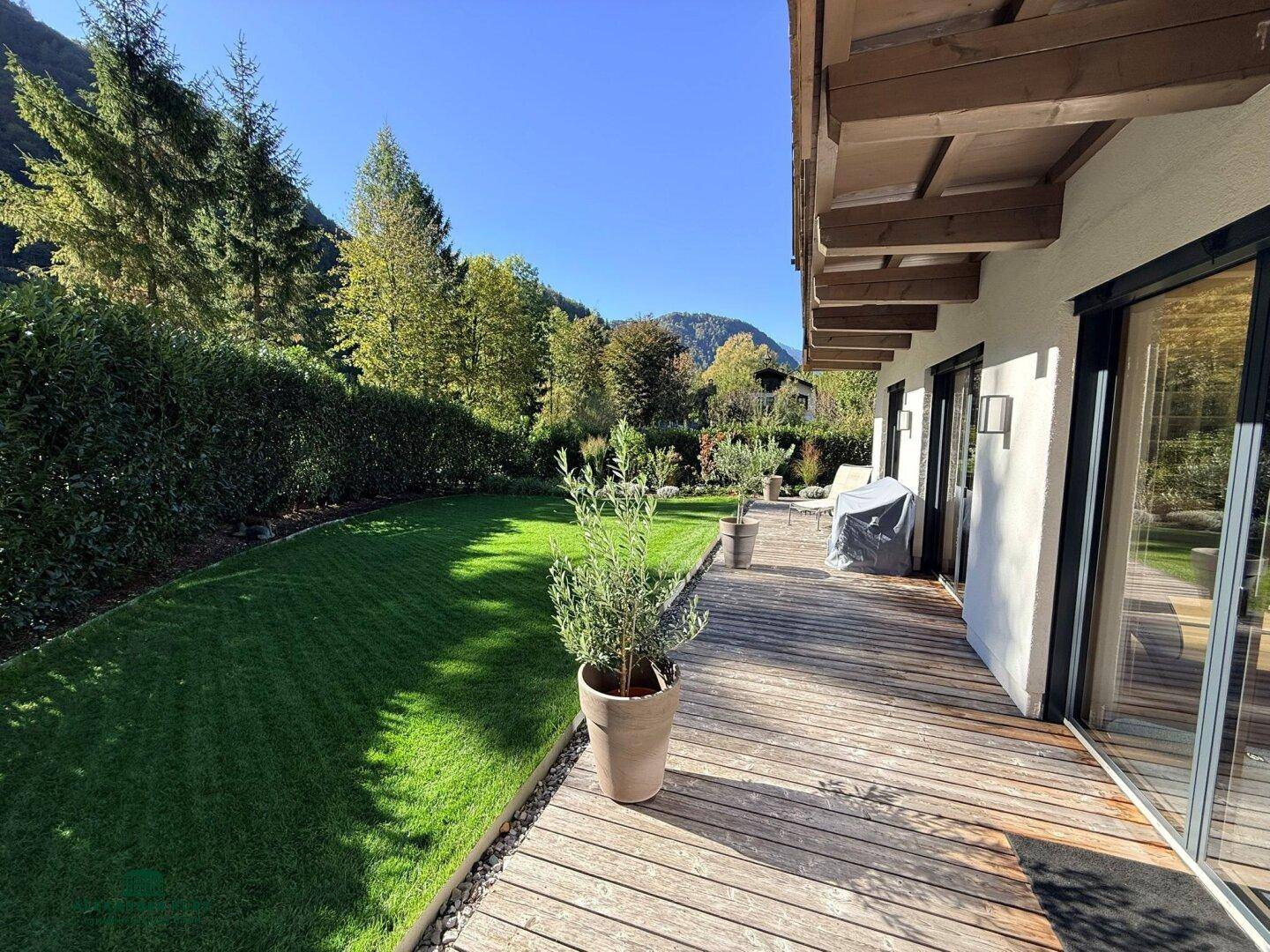 Gepflegter Garten mit großer Holzterrasse, Rasenfläche und Blick auf die Berge.