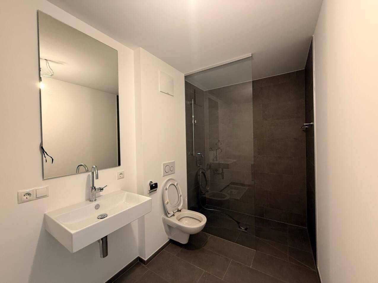 Modernes Badezimmer mit ebenerdiger Dusche, wandhängendem WC und großem Spiegel.