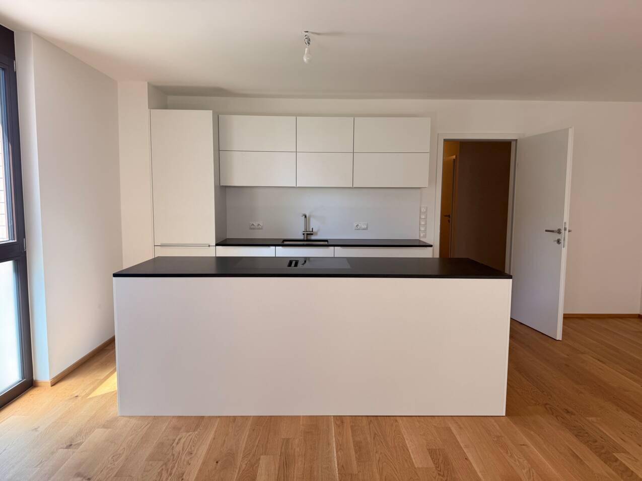 Moderne Einbauküche mit weißer Kücheninsel, dunkler Arbeitsplatte und hellem Holzfußboden.