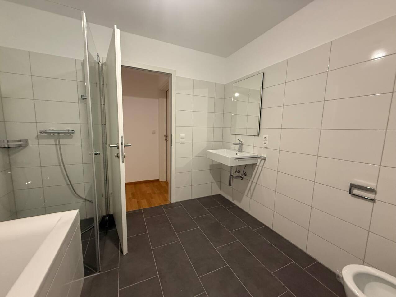 Modernes Badezimmer mit Badewanne, Dusche, Waschbecken und dunklen Bodenfliesen.