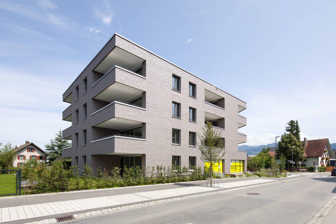 Modernes Wohngebäude mit Holzschindelfassade und Balkonen an einer ruhigen Straße gelegen.