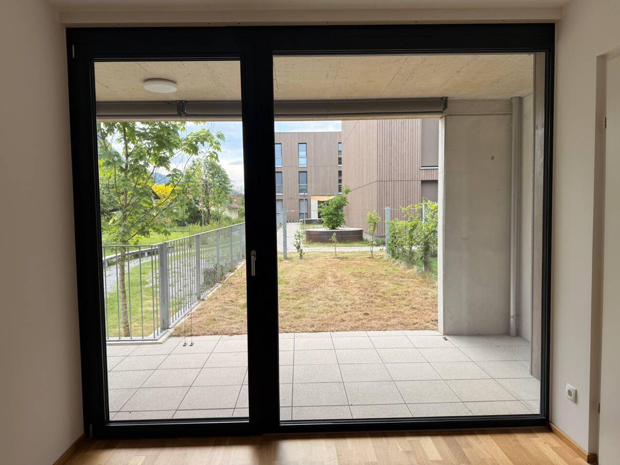 Große Schiebetür bietet Zugang zu einer gefliesten Terrasse mit Blick auf die Grünanlage.