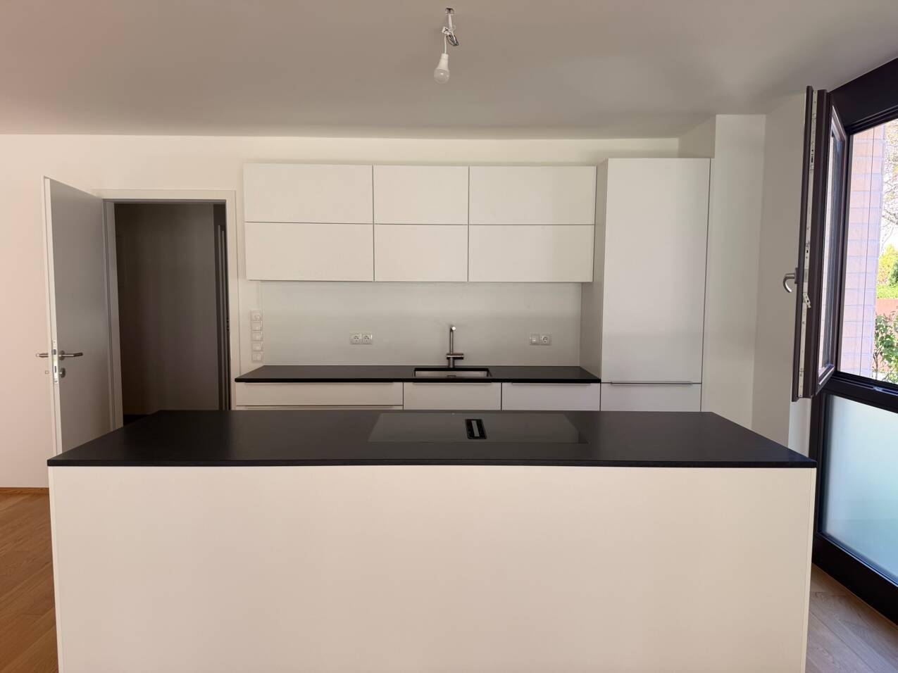 Moderne Einbauküche mit weißen Schränken, schwarzen Arbeitsplatten und einer Kochinsel.