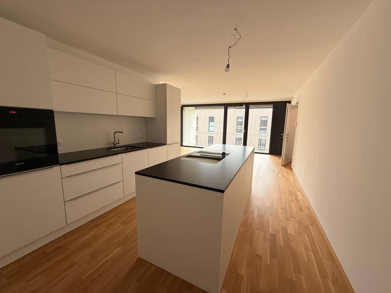 Helle, moderne Einbauküche mit Kochinsel, dunkler Arbeitsplatte und Holzboden.