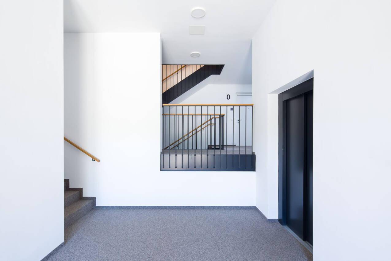 Heller Eingangsbereich mit Treppenhaus, Aufzug und modernem Design.