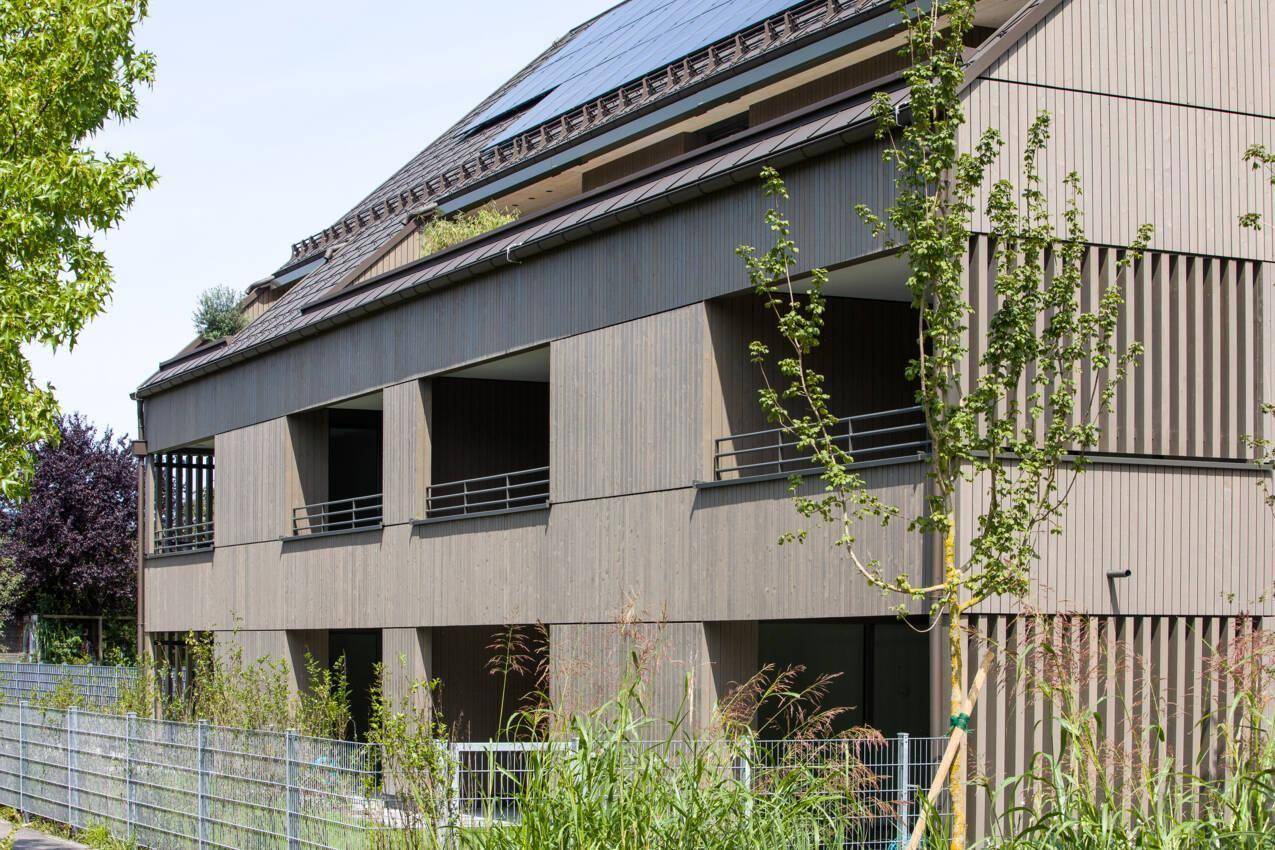 Detailansicht der modernen Holzfassade mit integrierten Loggien und Solaranlagen auf dem Dach.